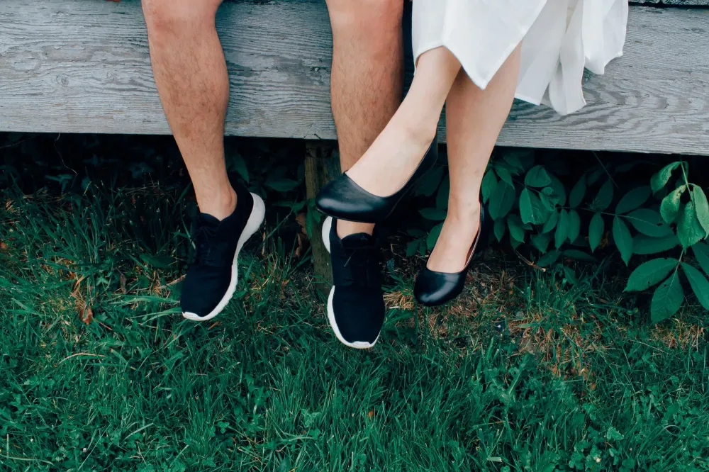 male and female sitting with grass background wearing sneakers and slip on shoe